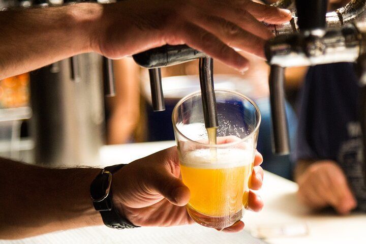 Bartender pouring beer into a pint glass, hands visible. Golden brew, white foam.