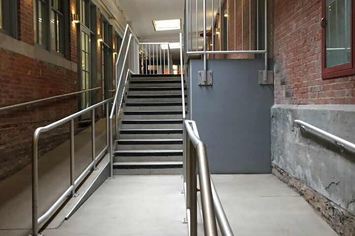 Indoor hallway with stairs, ramp, and metal handrails against brick walls.