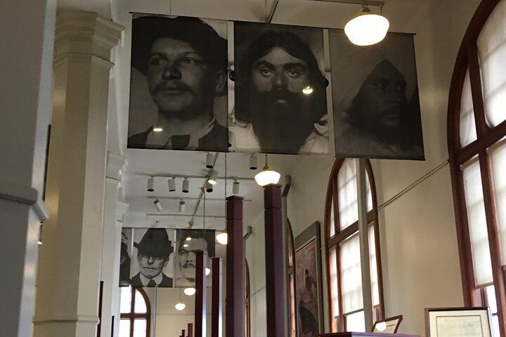 Portraits hanging in a corridor with arched windows. Three large, black and white portraits are visible.