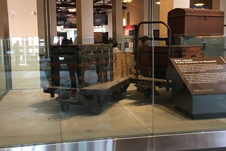 Vintage luggage on a rail cart inside a museum display case.