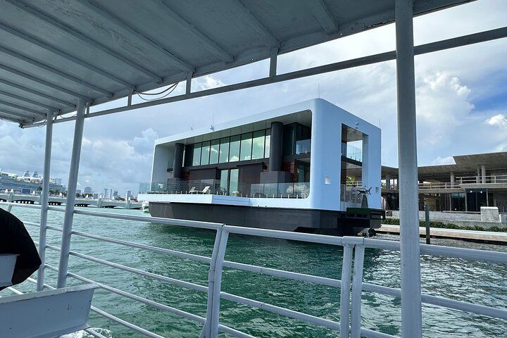 Modern floating house on water with glass windows and white frame. Viewed from a boat.