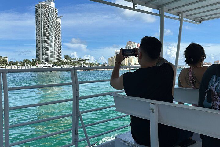 Person on boat taking photo of tall building near water. Blue sky and water.