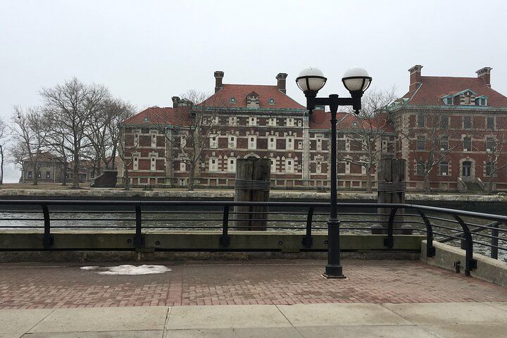 Waterfront view of brick buildings with red tile roofs and a lamppost on a brick and concrete pier.