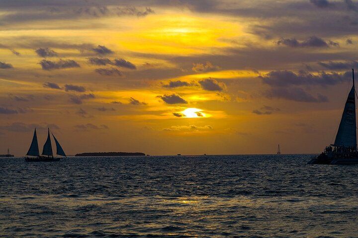 Sunset over ocean with sailboats silhouetted against a vibrant yellow and orange sky.