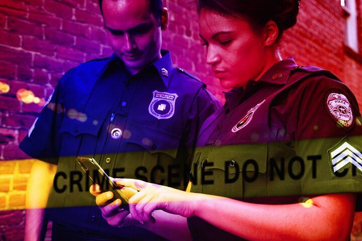 Two police officers examining a phone at a crime scene. Yellow tape reads 