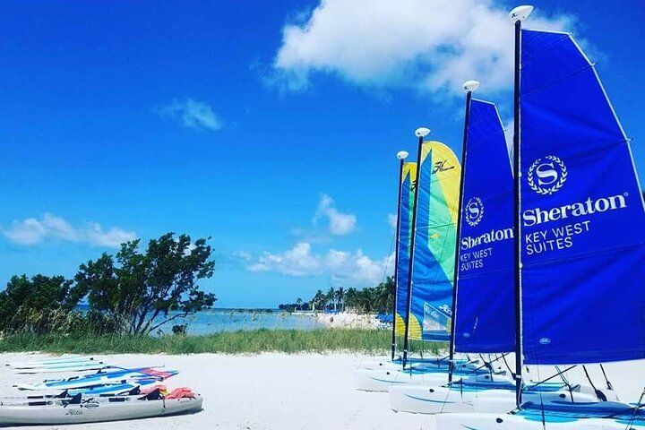 Blue sails on a white sandy beach under a blue sky, promoting Sheraton Key West Suites.