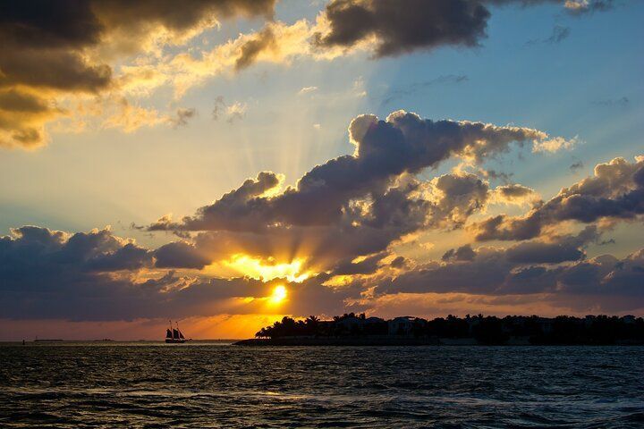 Sunset over the ocean, sun rays burst through clouds; a boat sails on the horizon.