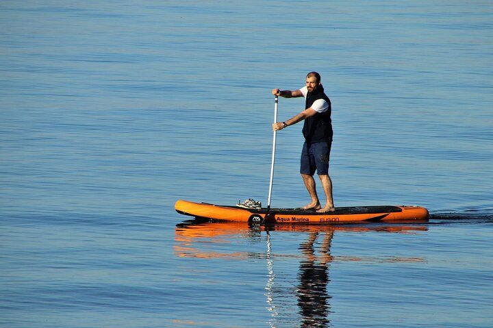 Man paddleboarding on an orange board in calm blue water.