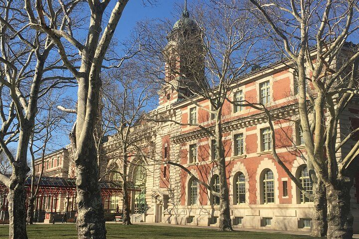 Brick building with tower, framed by bare trees, on a sunny day.