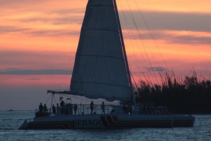 Sailboat with passengers silhouetted against a sunset sky.