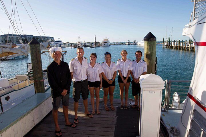 Group of seven people posing on a dock. They are near a boat and water in the background.
