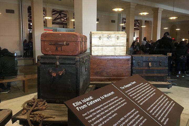 Suitcases and trunks at Ellis Island museum. Brown, black, and white luggage with informational sign in a large hall.