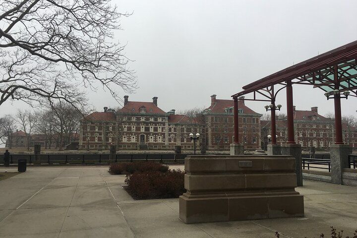Large brick building with multiple sections and red roofs. A cloudy, overcast sky.