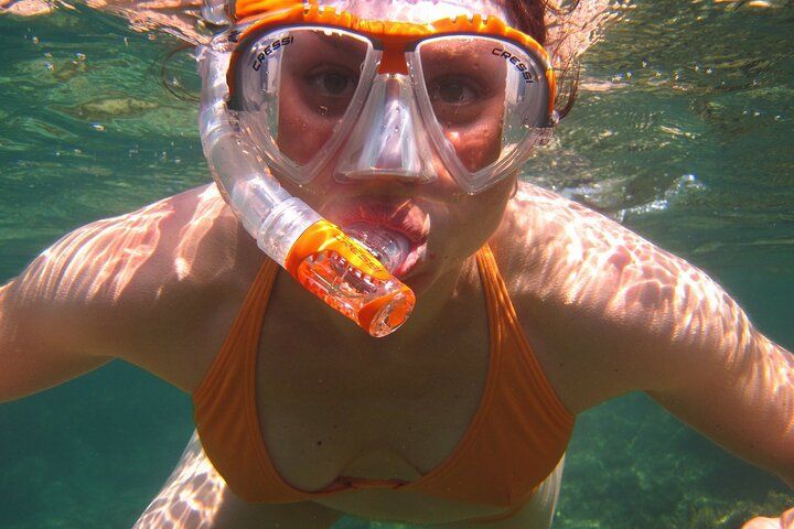 Woman snorkeling underwater, wearing orange bikini and snorkel, with a close-up view.