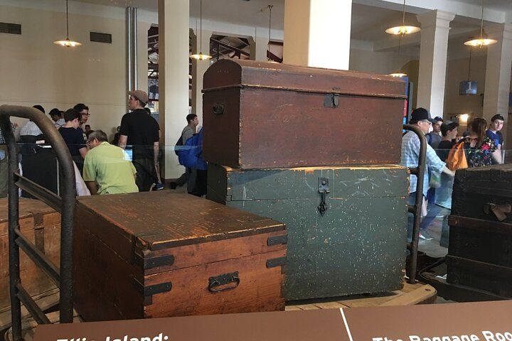 Three old wooden trunks stacked in a museum exhibit; people in the background.