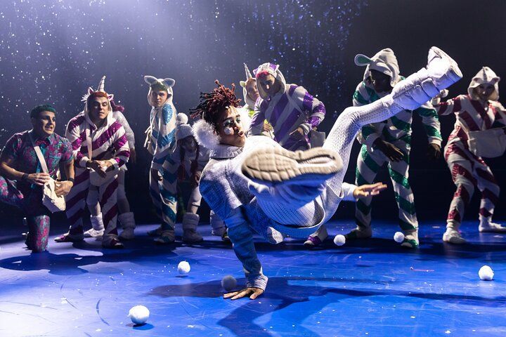 A dancer doing a freeze, in front of costumed performers. Snow effect on a blue stage.