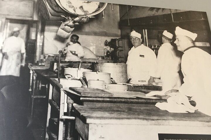 Kitchen with several chefs in white uniforms working near counters and large pots.