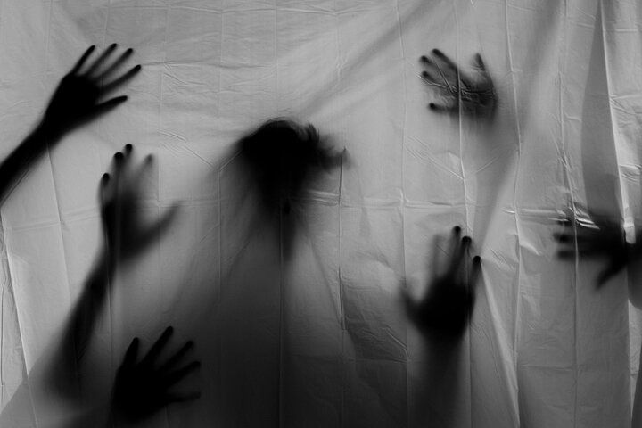 Hands press against a translucent fabric, obscuring a central shadowy figure. Black and white.