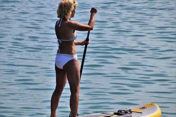 Woman on a paddleboard in a bikini paddles on blue water.