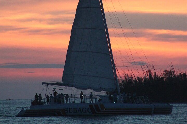 Sailboat at sunset with passengers silhouetted against a colorful sky.