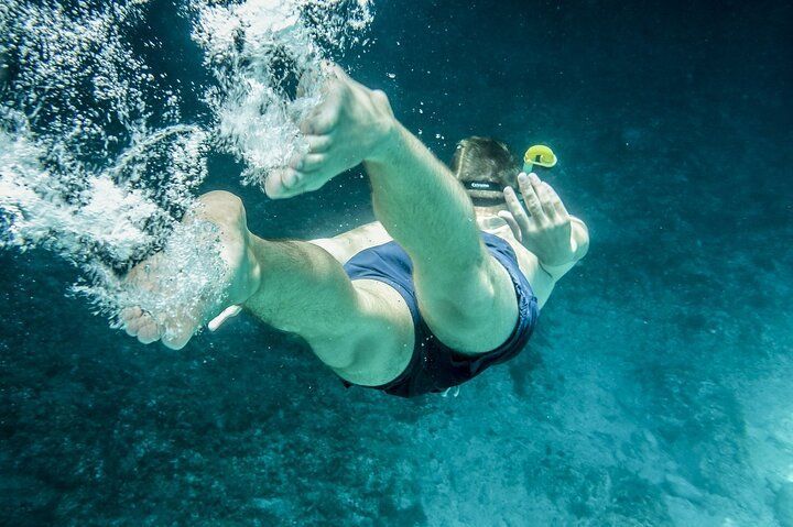 Person snorkeling underwater, wearing blue shorts, reaching out.
