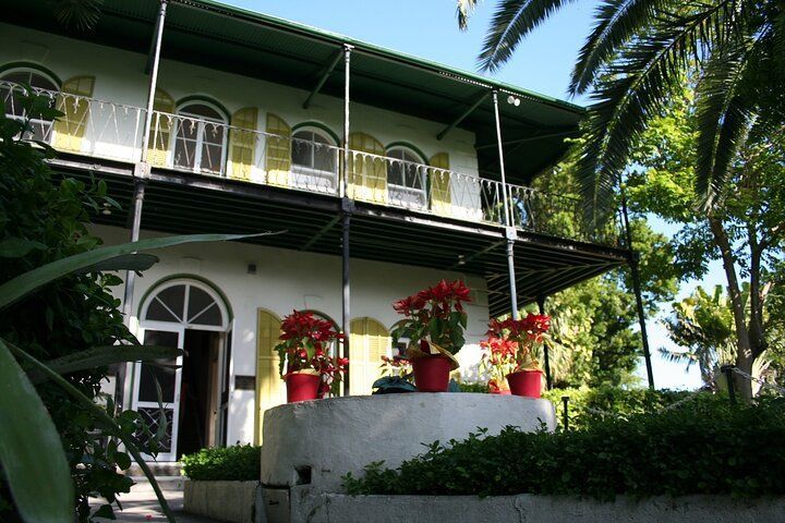 White two-story house with yellow shutters, green balcony, red flowers in Key West, Florida.