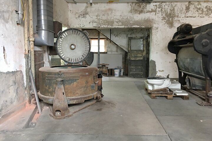 Rusty industrial machinery in a decaying workshop, with a doorway and exposed pipes.