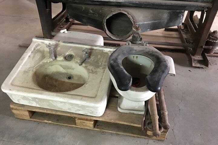 Old bathroom fixtures, including a toilet and sink, on a wooden pallet next to a large metal structure.