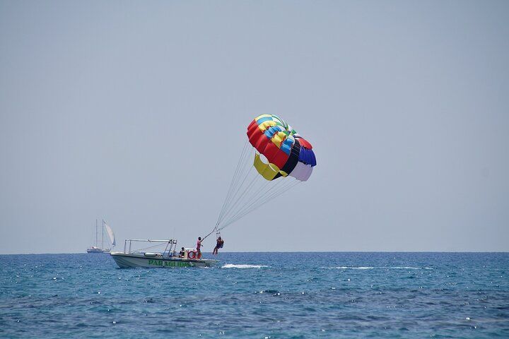 Parasailing over ocean with a colorful parachute and a boat in the background. Bright sunny day.