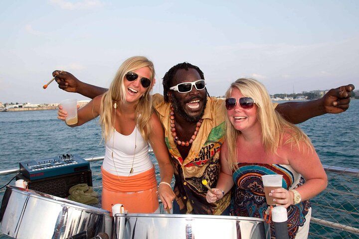 Three people on a boat smiling at the camera; a man playing steel drums with two women.