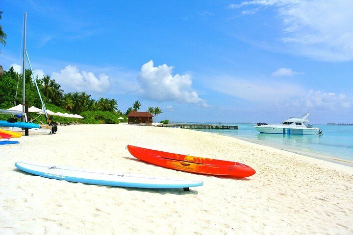 White sand beach with kayaks, calm blue water, and a boat under a bright blue sky.