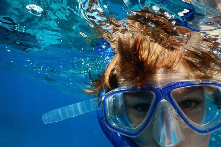 Person snorkeling underwater, wearing blue mask and snorkel; water is blue, sunny day.