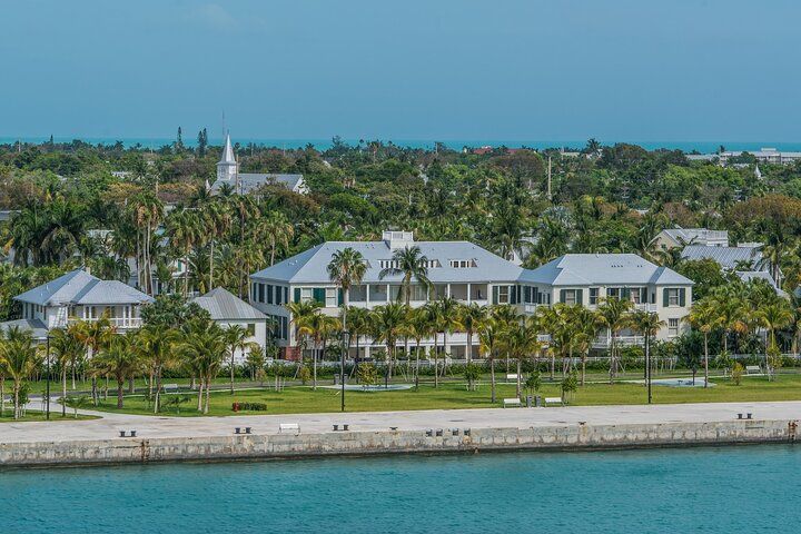 Large white building with green shutters near water and palm trees in Key West.