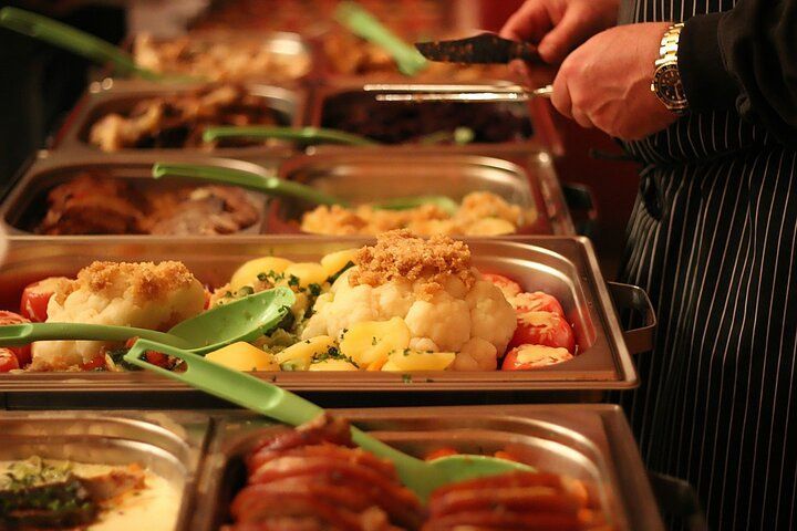 Buffet of various dishes, a person with tongs serving food from a stainless steel tray.