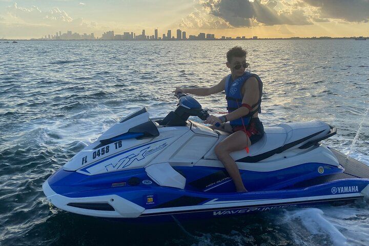 Person on a blue and white jet ski on water, with a city skyline in the distance.