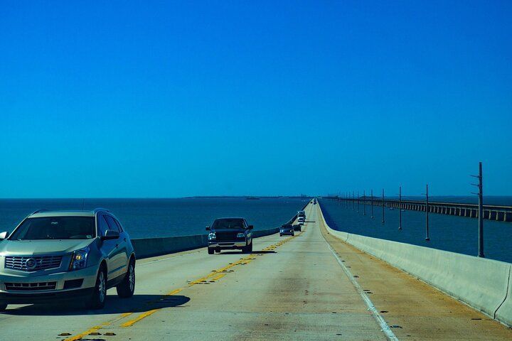 Cars driving on a long bridge over the ocean under a clear blue sky.