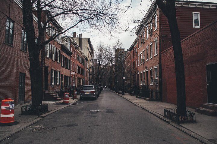 Narrow city street lined with brick buildings, bare trees, and a parked car.
