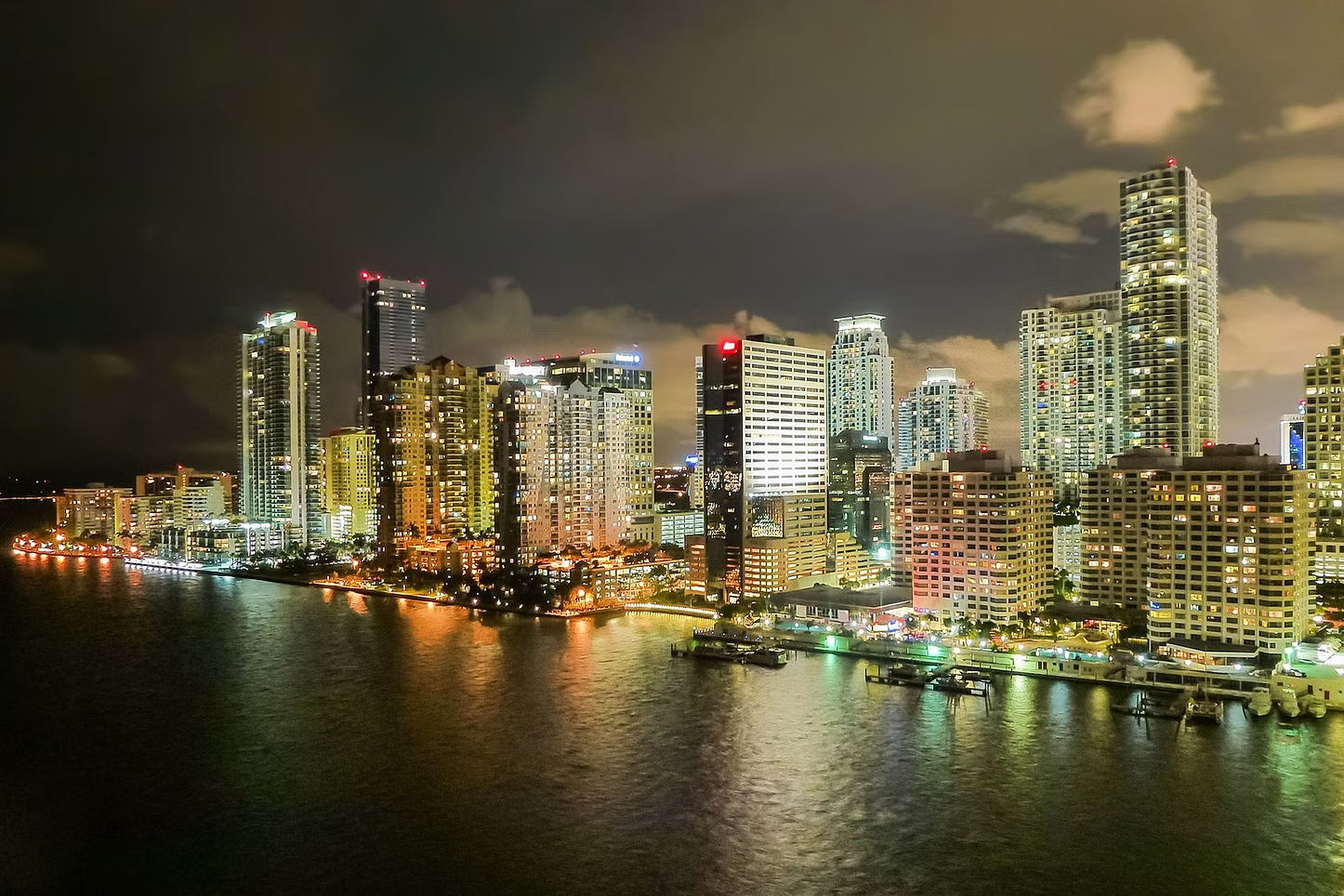 City skyline at night, brightly lit buildings reflected in the water.