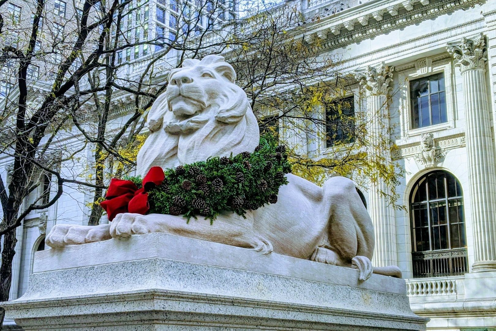 Sculpture of a lion wearing a wreath and roses in front of the New York Public Library building.