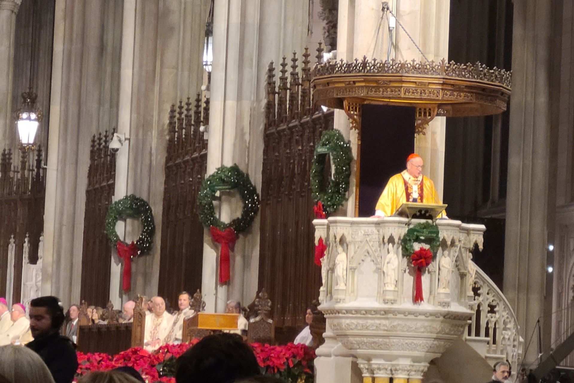 A cardinal giving a sermon from a decorated pulpit during a Christmas service.
