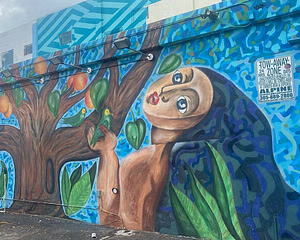 Mural of woman with a tree, oranges, and parrots on a blue and green background.