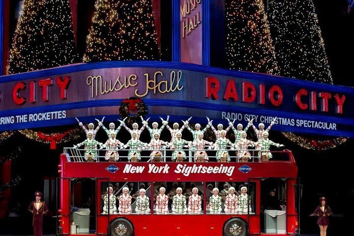 Rockettes on a red double-decker bus in front of Radio City Music Hall, part of the Christmas Spectacular.