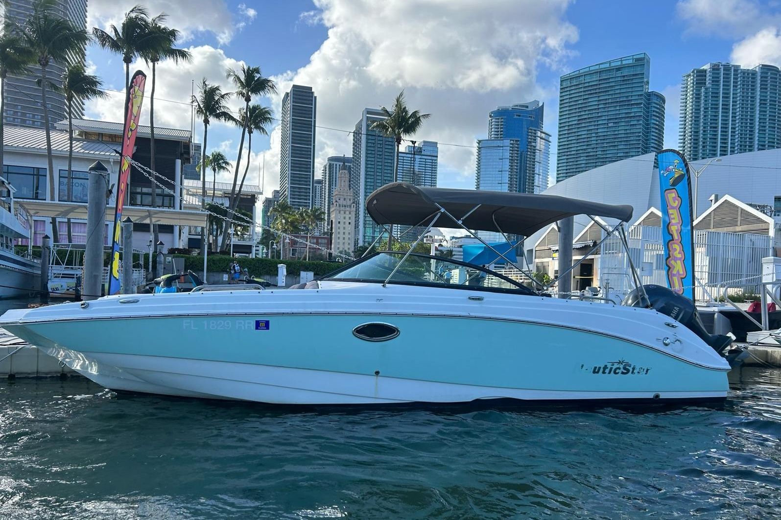 A teal and white motorboat docked in a marina with city skyscrapers in the background.
