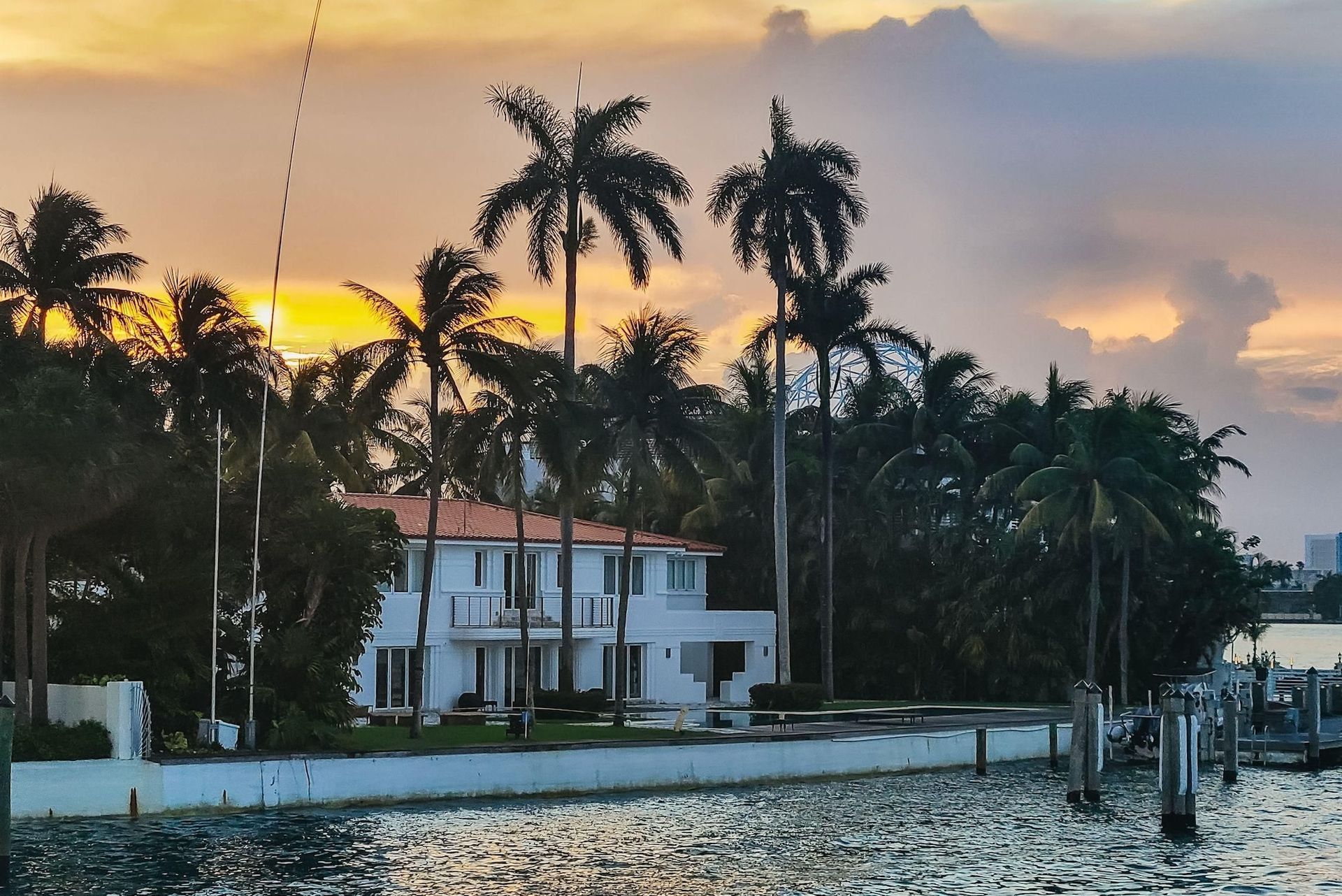 House with palm trees at sunset over water.