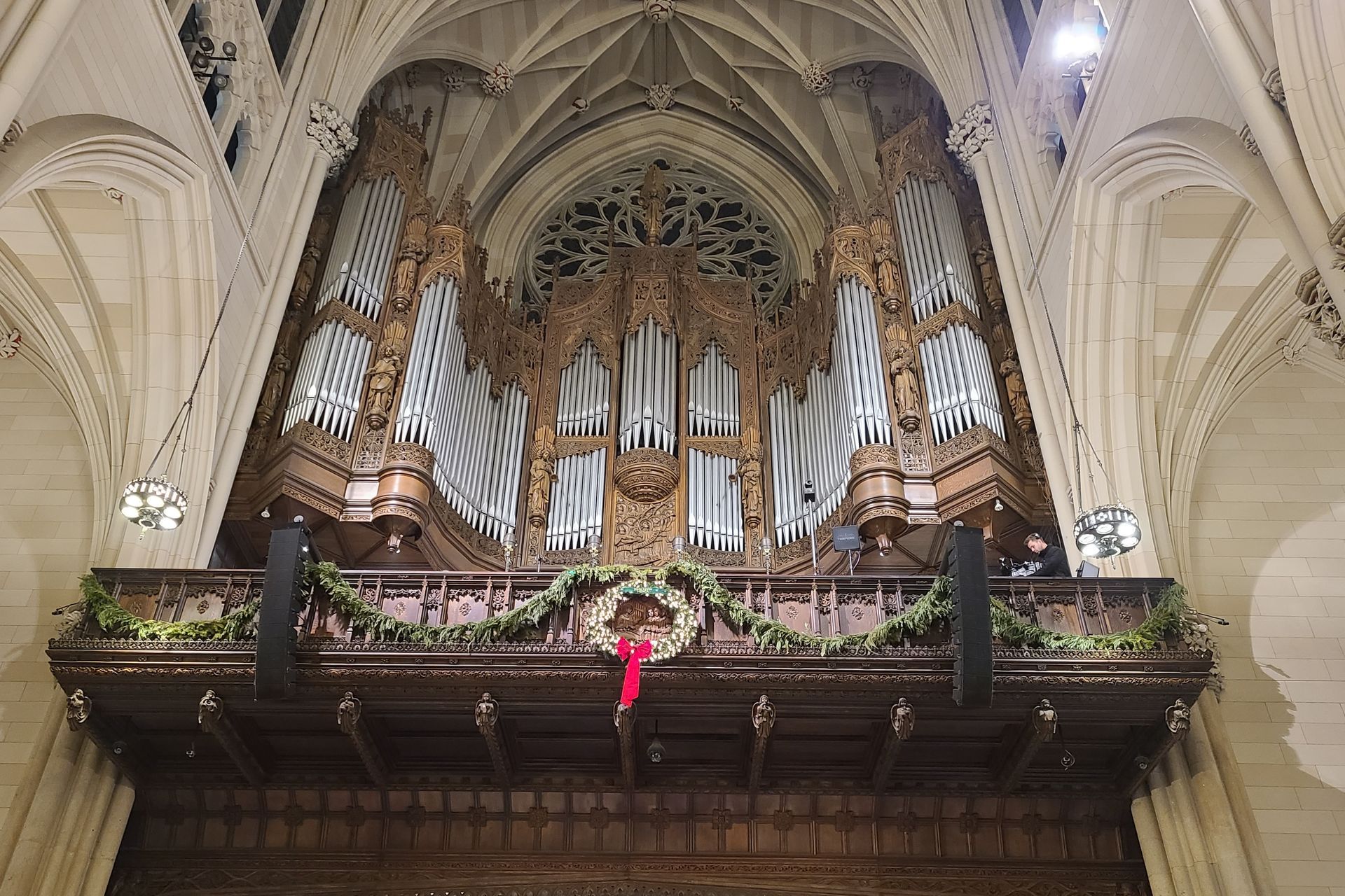 A large pipe organ decorated with greenery and a red bow, inside a cathedral.
