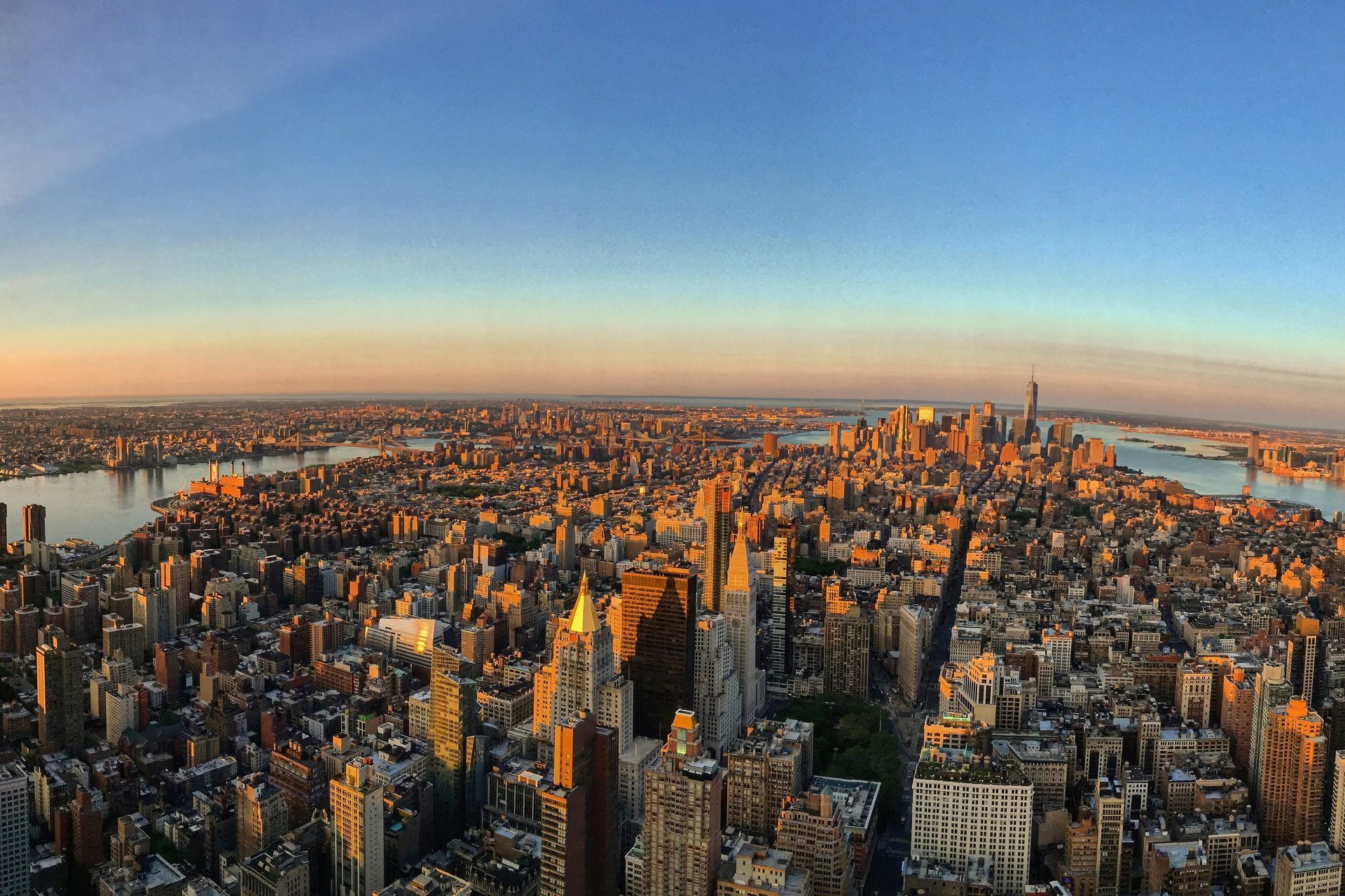 Aerial view of New York City buildings at sunset. Golden light illuminates the city skyline and waterways.