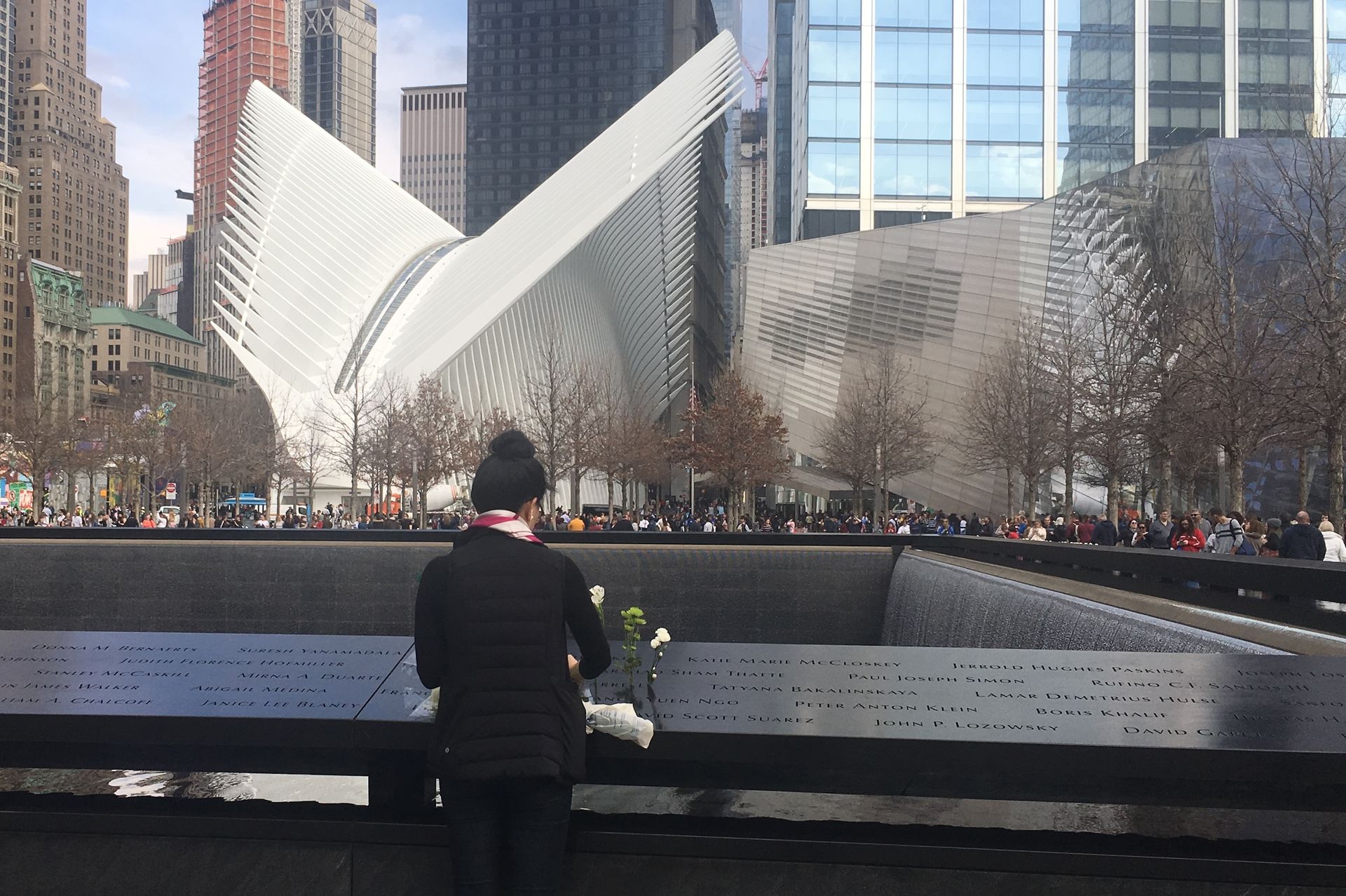 Person places flowers at the 9/11 Memorial in NYC, with the Oculus building in the background.