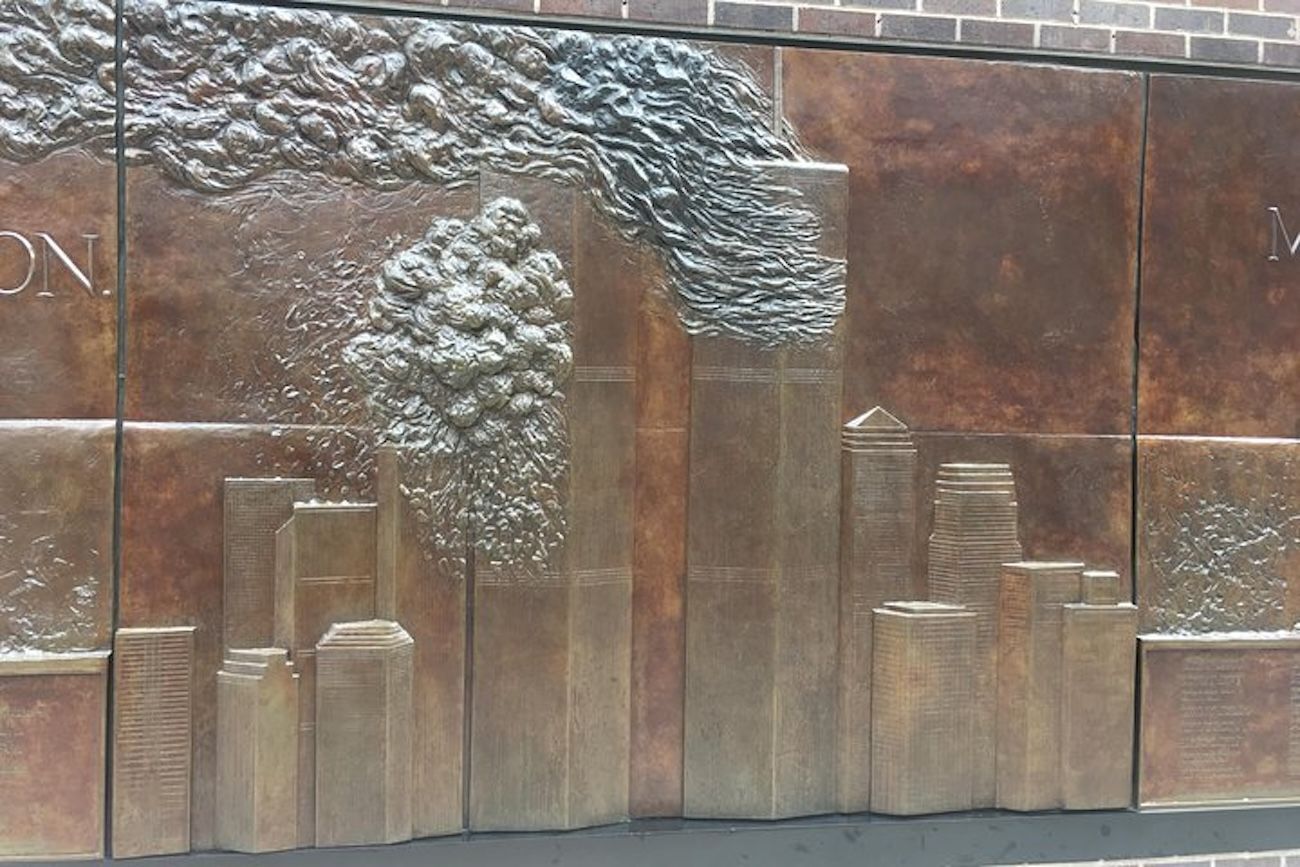 Bronze relief depicting the New York City skyline with the Twin Towers engulfed in smoke, a memorial.