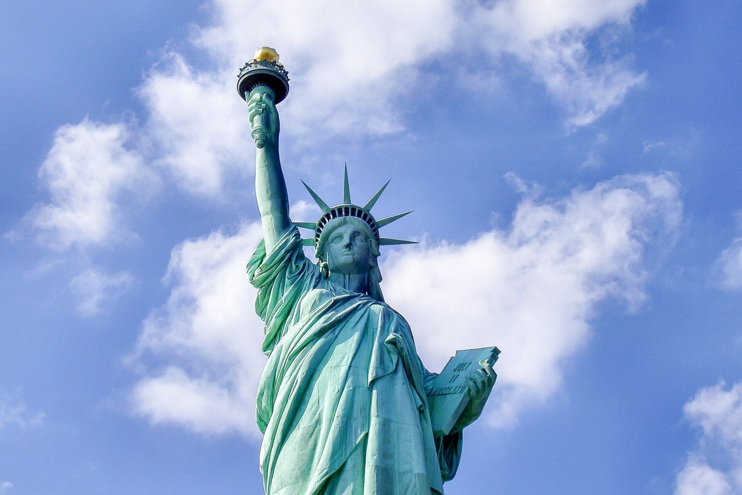 Statue of Liberty with a torch, against a blue sky with white clouds.