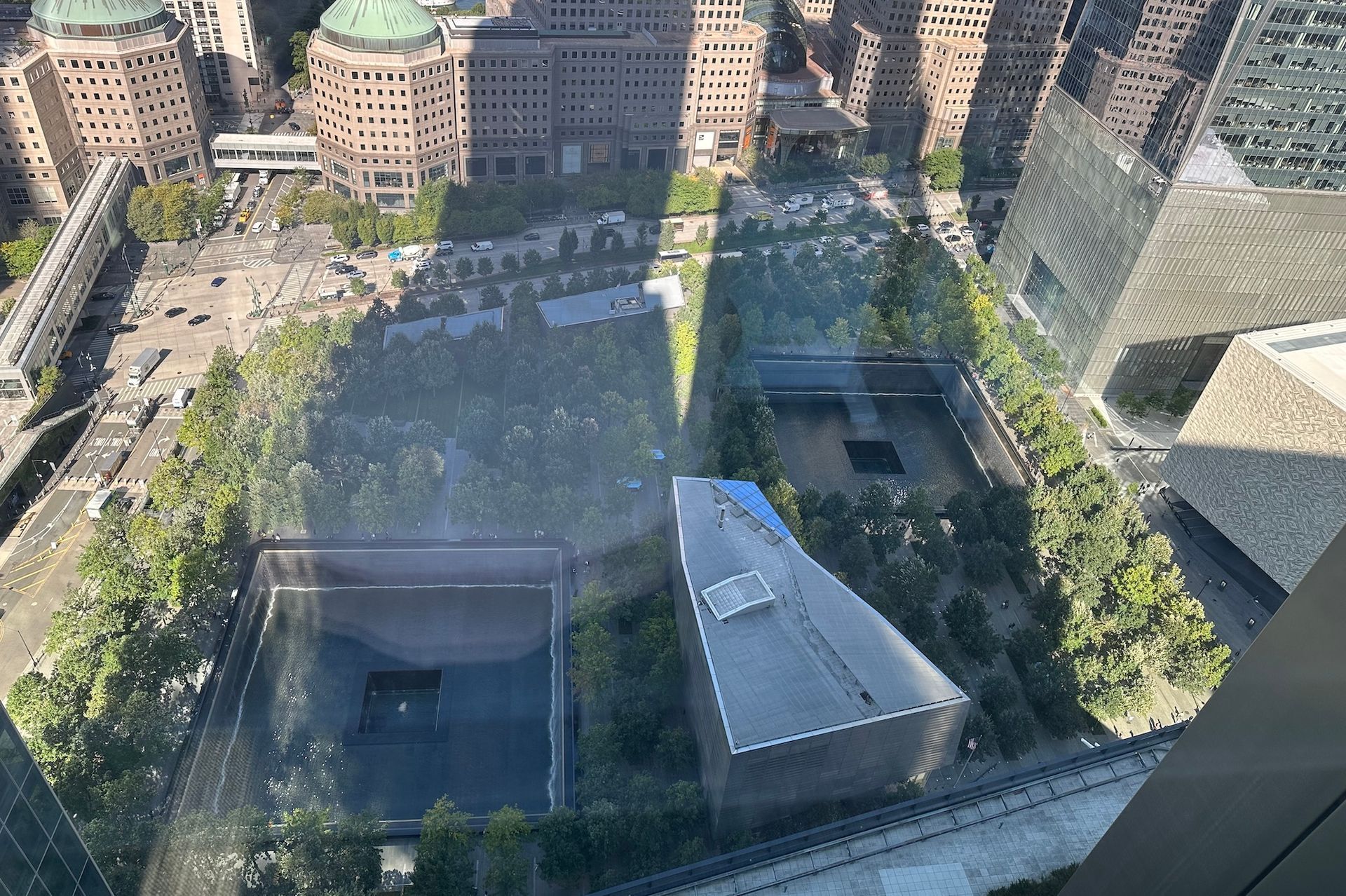 Aerial view of the 9/11 Memorial and Museum in New York City. Two reflecting pools, surrounded by green space and buildings.